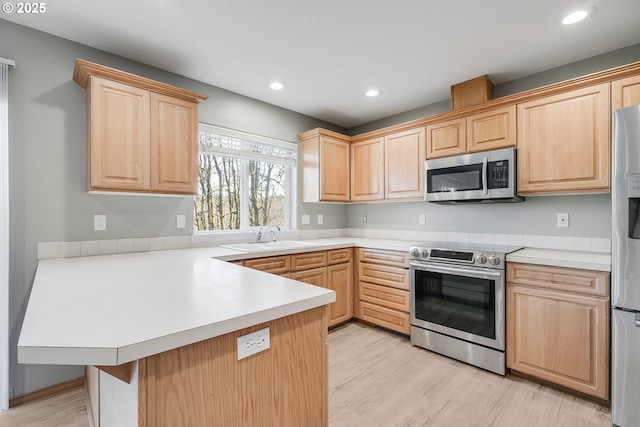 kitchen with stainless steel appliances, sink, light brown cabinets, and kitchen peninsula