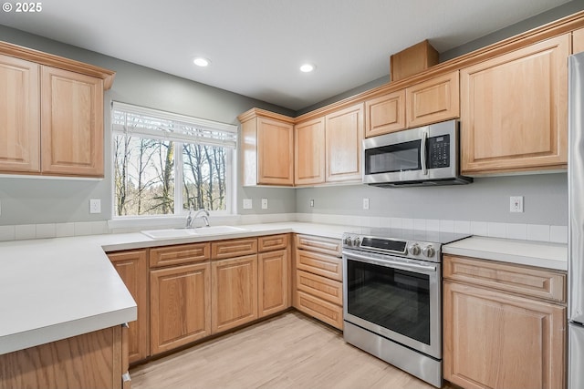 kitchen featuring light brown cabinetry, sink, light hardwood / wood-style flooring, and appliances with stainless steel finishes