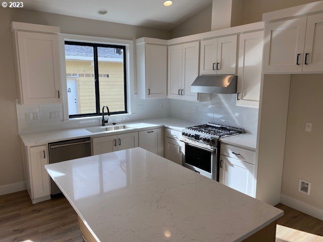 486 Meadows Dr, Manzanita, OR 97130 - kitchen with under cabinet range hood, appliances with stainless steel finishes, decorative backsplash, a center island, and wood finished floors