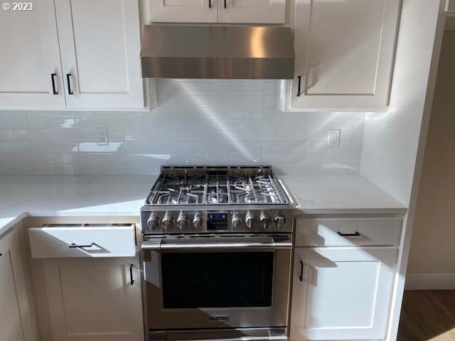 486 Meadows Dr, Manzanita, OR 97130 - kitchen featuring under cabinet range hood, stainless steel gas range oven, white cabinetry, backsplash, and light stone countertops