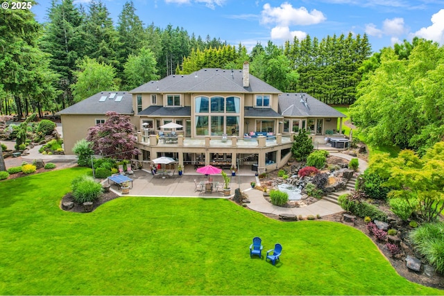 rear view of property featuring a balcony, a lawn, and a patio area