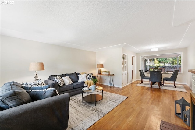 living area with light wood-style flooring, baseboards, and a textured ceiling