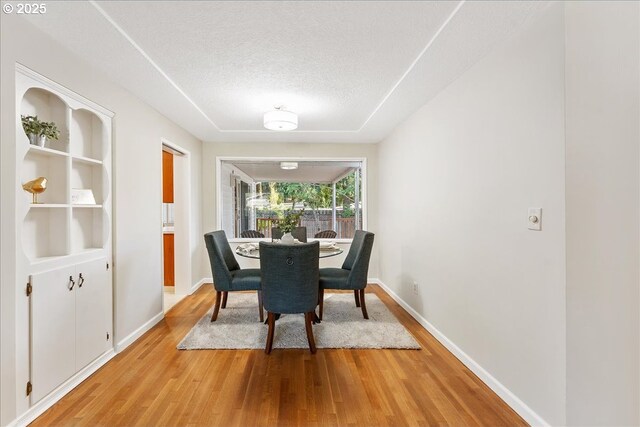 dining space with light wood finished floors, a textured ceiling, and baseboards