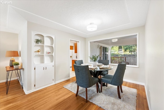 dining space featuring light wood-style flooring, a textured ceiling, and baseboards