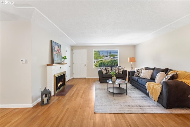 living area featuring light wood-type flooring, baseboards, a textured ceiling, and a brick fireplace
