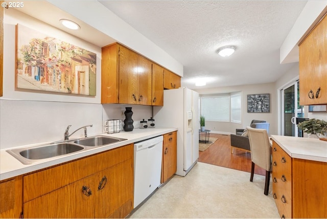 kitchen with white appliances, a sink, light countertops, brown cabinetry, and a textured ceiling