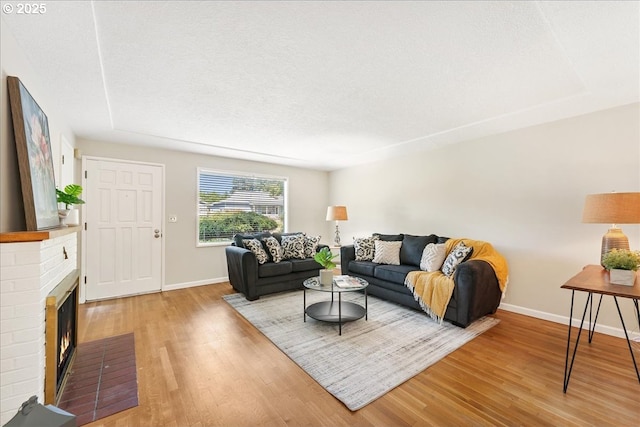 living room featuring baseboards, light wood-style flooring, and a fireplace