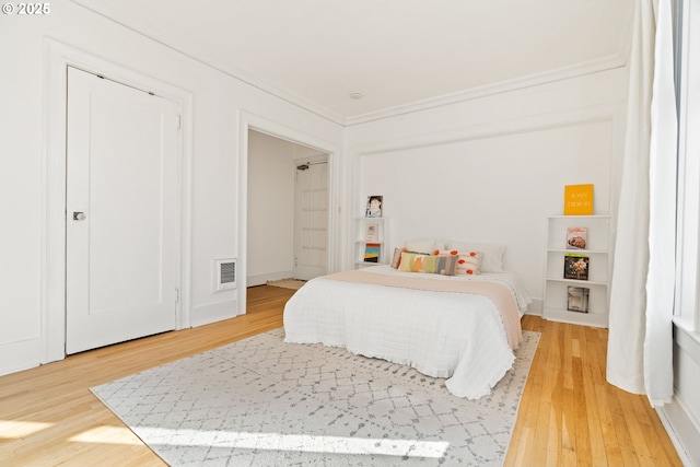 bedroom featuring baseboards, ornamental molding, visible vents, and light wood-style floors