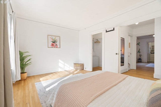 bedroom featuring baseboards, a spacious closet, wood finished floors, and crown molding