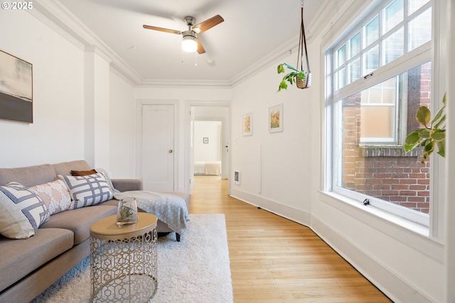 living room with light wood-type flooring, baseboards, ornamental molding, and a ceiling fan