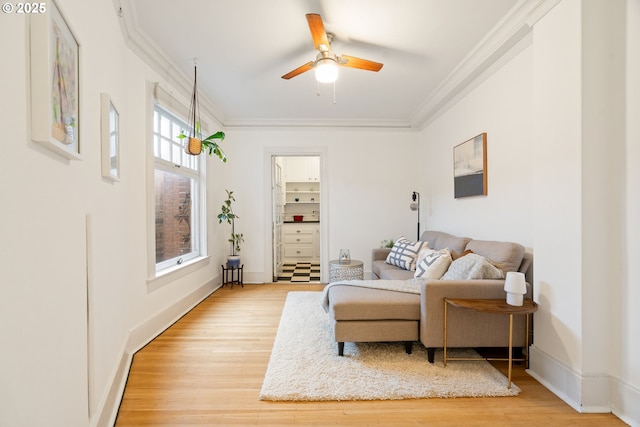 living area featuring baseboards, light wood-style floors, a ceiling fan, and crown molding