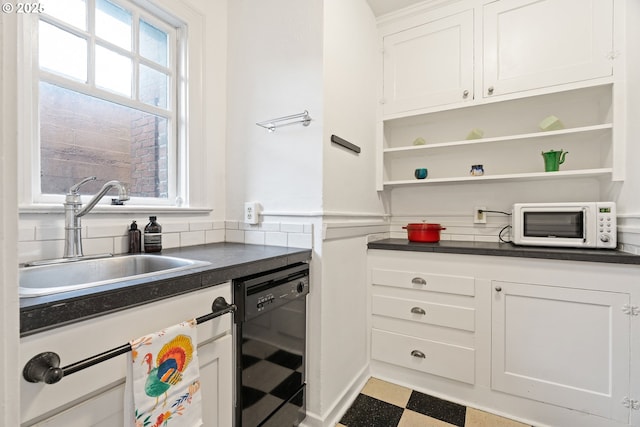 kitchen featuring dark countertops, white microwave, black dishwasher, and a sink