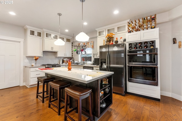 kitchen with white cabinets, hanging light fixtures, light wood-type flooring, appliances with stainless steel finishes, and a kitchen island