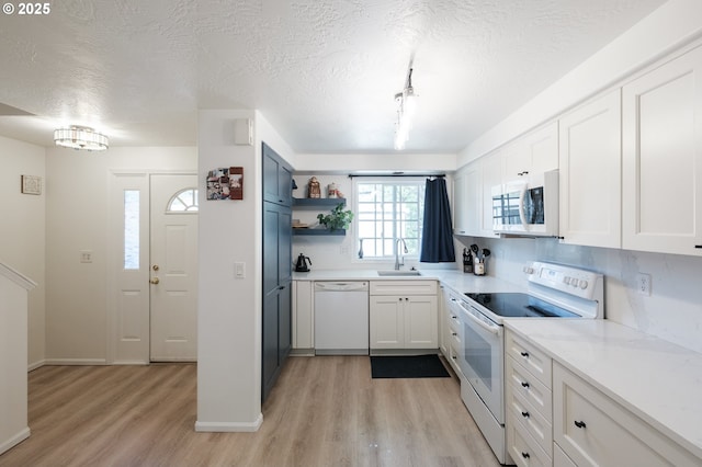 kitchen with white appliances, light wood-style floors, a sink, white cabinetry, and a textured ceiling
