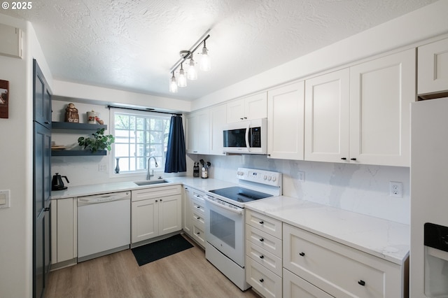 kitchen with white appliances, a sink, a textured ceiling, light wood-type flooring, and white cabinets