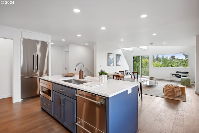 kitchen with sink, built in appliances, a kitchen island with sink, and dark wood-type flooring