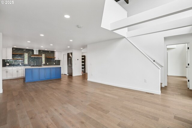 kitchen with white cabinets, high end fridge, an island with sink, and wall chimney range hood