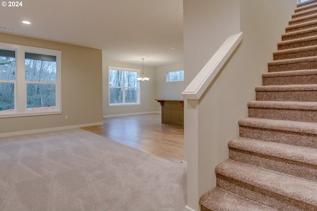 staircase with an inviting chandelier and carpet floors