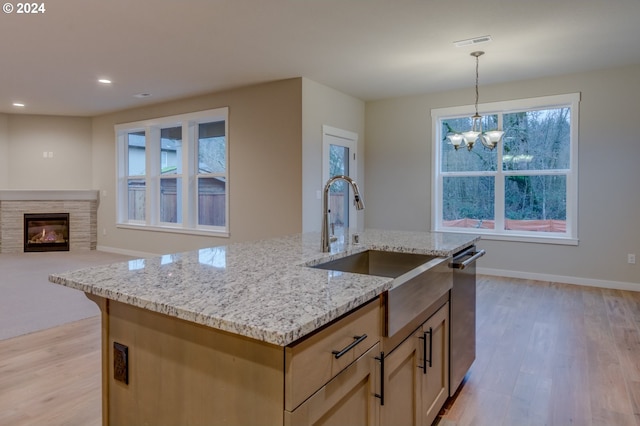 kitchen featuring light hardwood / wood-style floors, stainless steel dishwasher, decorative light fixtures, light stone counters, and a center island with sink