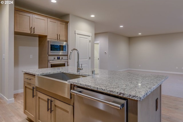 kitchen with light brown cabinetry, appliances with stainless steel finishes, sink, light stone counters, and an island with sink