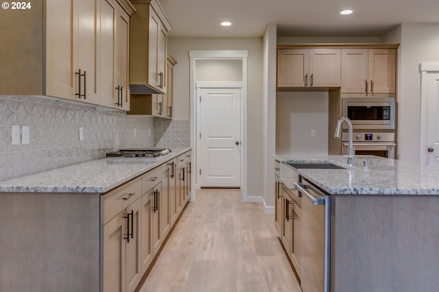 kitchen with sink, light wood-type flooring, tasteful backsplash, light stone counters, and stainless steel appliances