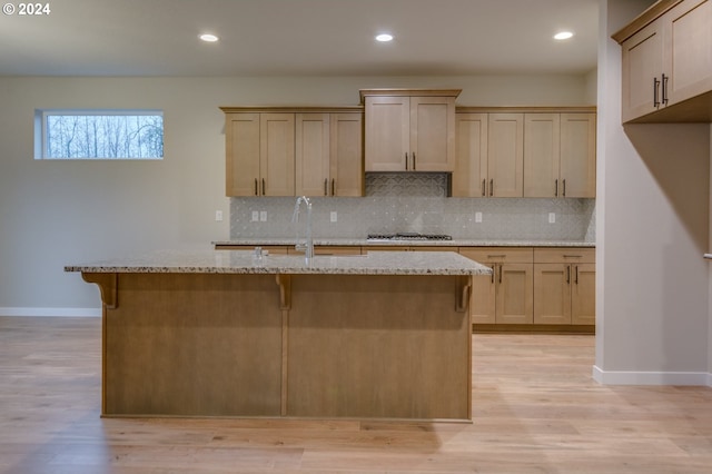 kitchen with a center island with sink, light brown cabinetry, and light stone counters