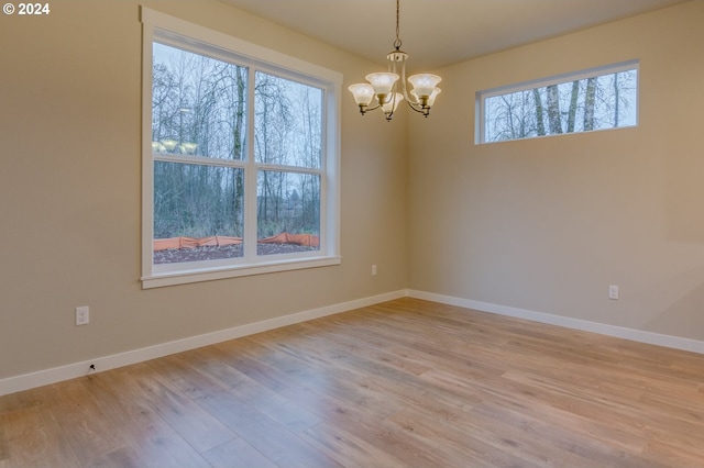 spare room featuring a chandelier, plenty of natural light, and light hardwood / wood-style flooring