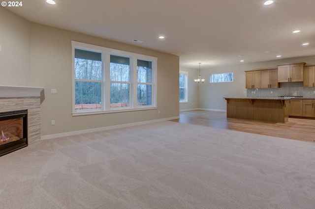 unfurnished living room with a notable chandelier, light carpet, and a tiled fireplace