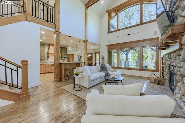 living room with a stone fireplace, stairs, a wealth of natural light, and high vaulted ceiling