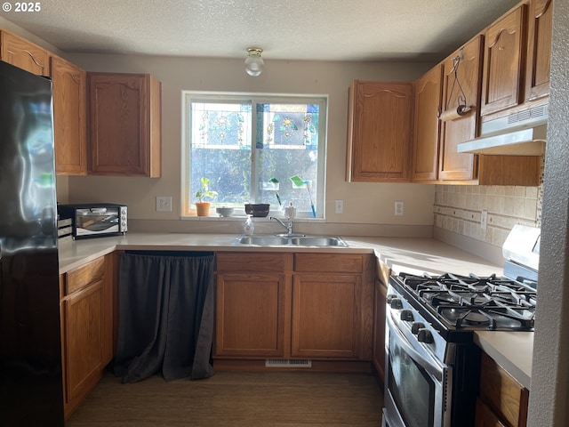 kitchen with wood-type flooring, sink, backsplash, stainless steel appliances, and a textured ceiling