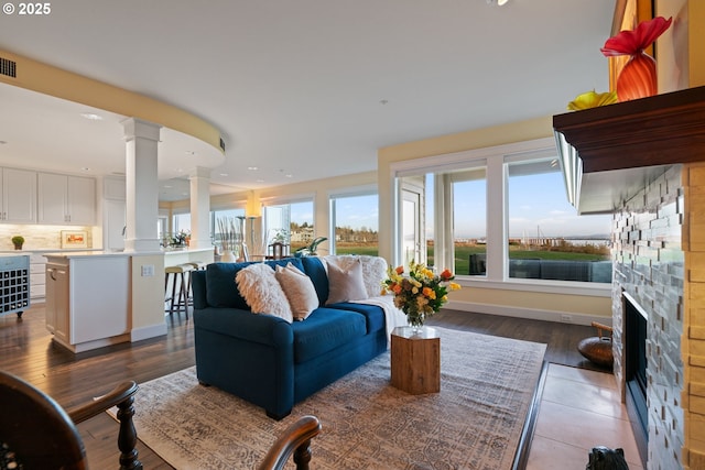 living area with recessed lighting, a fireplace, baseboards, dark wood-style flooring, and ornate columns