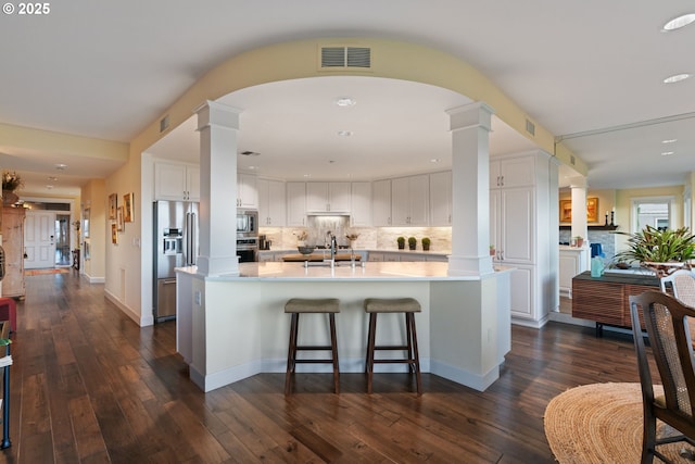 kitchen featuring visible vents, light countertops, decorative columns, stainless steel appliances, and white cabinetry