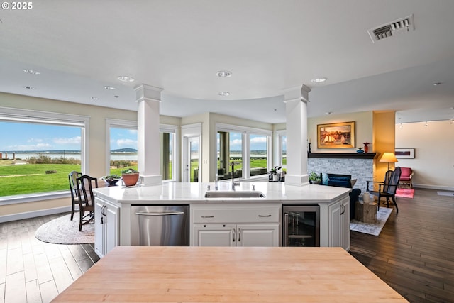 kitchen with visible vents, beverage cooler, open floor plan, ornate columns, and a sink