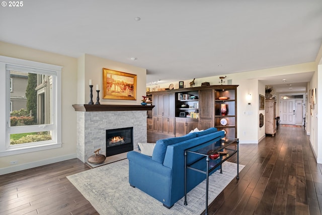 living area featuring a stone fireplace, dark wood-style floors, and baseboards