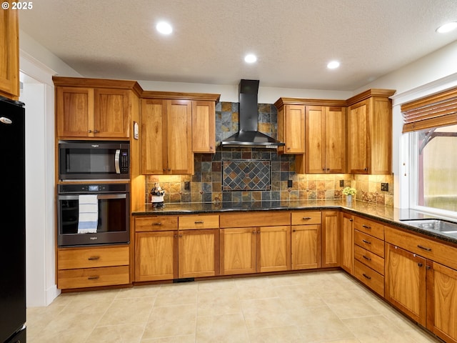 kitchen featuring a textured ceiling, wall chimney range hood, brown cabinets, black appliances, and tasteful backsplash