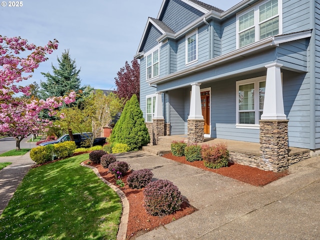 view of front of home with covered porch, stone siding, and a front yard