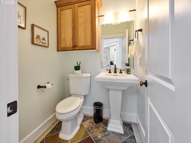 half bath featuring toilet, baseboards, and a sink