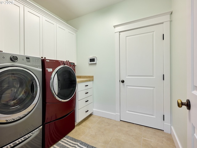 clothes washing area featuring baseboards, separate washer and dryer, light tile patterned floors, and cabinet space