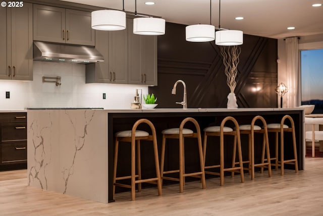 kitchen featuring under cabinet range hood, a sink, recessed lighting, light wood-style floors, and a breakfast bar