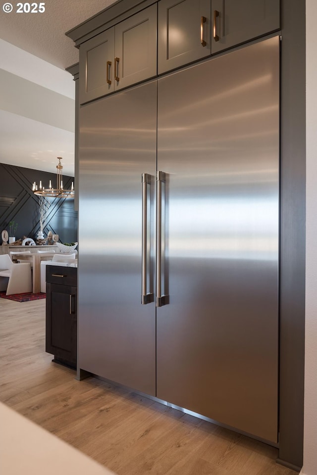 detailed view of stainless steel built in fridge, light wood-type flooring, a chandelier, and gray cabinetry