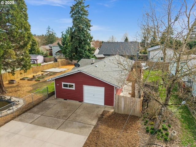 view of front facade featuring driveway, a shingled roof, an outdoor structure, and fence