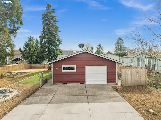 detached garage featuring concrete driveway and fence