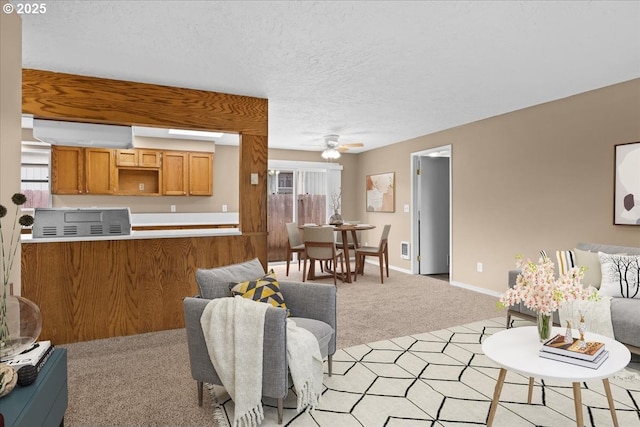 living area featuring ceiling fan, a textured ceiling, light carpet, baseboards, and a wall mounted AC