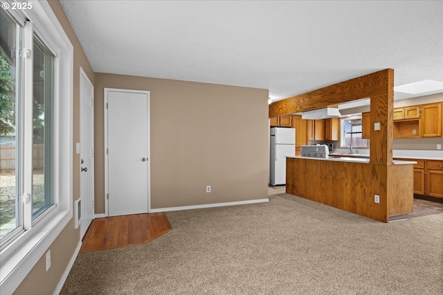 kitchen with light carpet, baseboards, brown cabinetry, freestanding refrigerator, and a sink