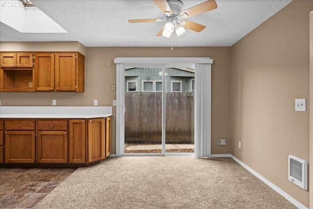 kitchen with light countertops, brown cabinetry, a skylight, and baseboards