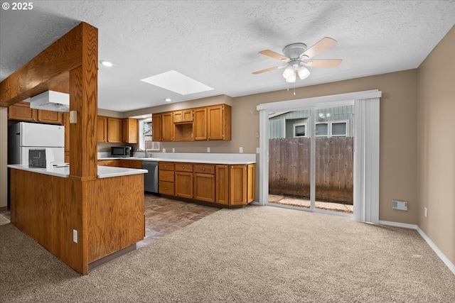 kitchen with a skylight, dishwasher, brown cabinets, freestanding refrigerator, and carpet floors