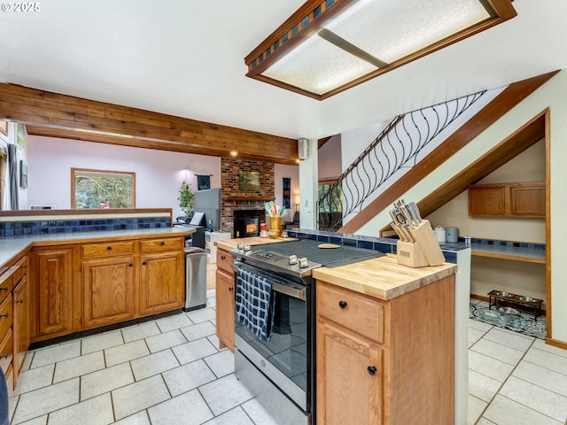 kitchen with a brick fireplace, butcher block countertops, open floor plan, stainless steel range with electric cooktop, and light tile patterned flooring