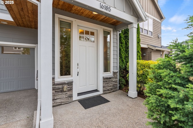 16185 NW Ashfield Dr, Beaverton, OR 97006 - view of exterior entry featuring board and batten siding, stone siding, a garage, and a porch