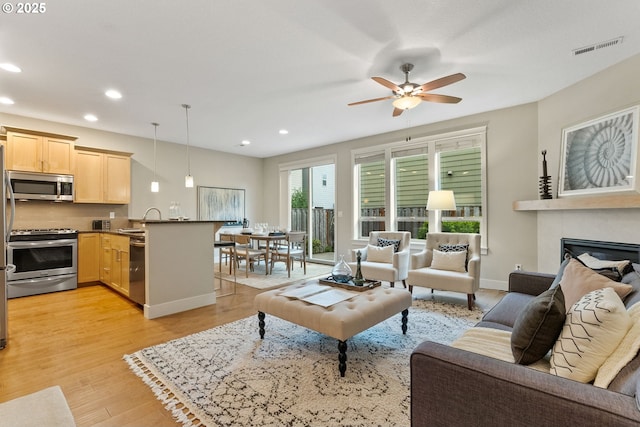 16185 NW Ashfield Dr, Beaverton, OR 97006 - living room with recessed lighting, a ceiling fan, light wood-style floors, a glass covered fireplace, and baseboards