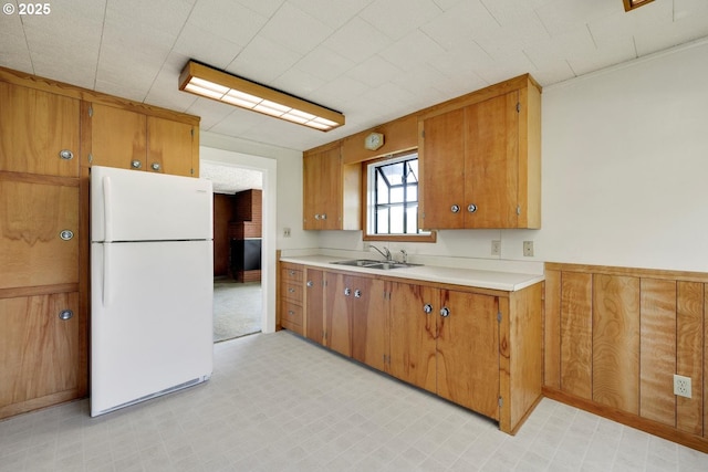 kitchen featuring brown cabinetry, a sink, light countertops, freestanding refrigerator, and light floors